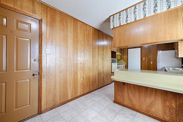 kitchen featuring white oven, light floors, wood walls, and freestanding refrigerator