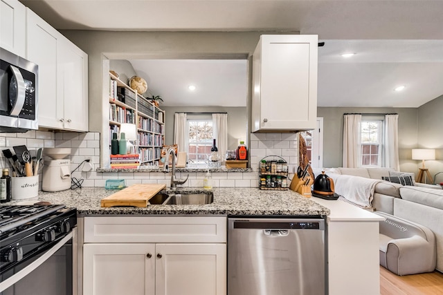 kitchen with light stone counters, appliances with stainless steel finishes, open floor plan, white cabinets, and a sink