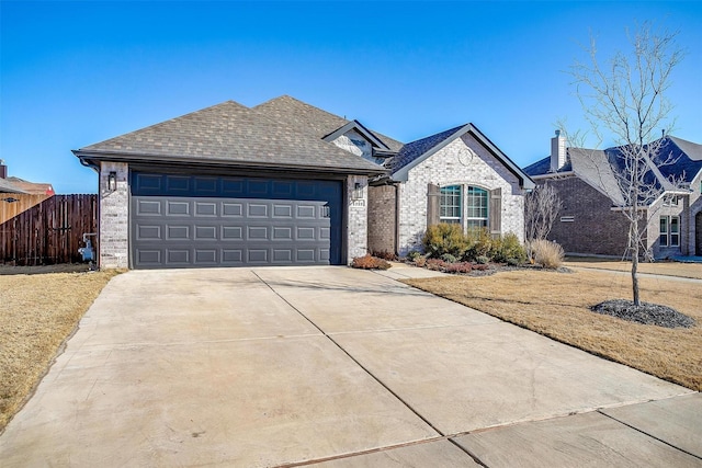 view of front of property featuring a garage, concrete driveway, roof with shingles, fence, and brick siding