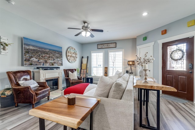 living area with recessed lighting, light wood-style flooring, a ceiling fan, and a glass covered fireplace