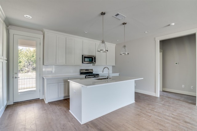 kitchen with decorative light fixtures, a center island with sink, light countertops, appliances with stainless steel finishes, and white cabinetry