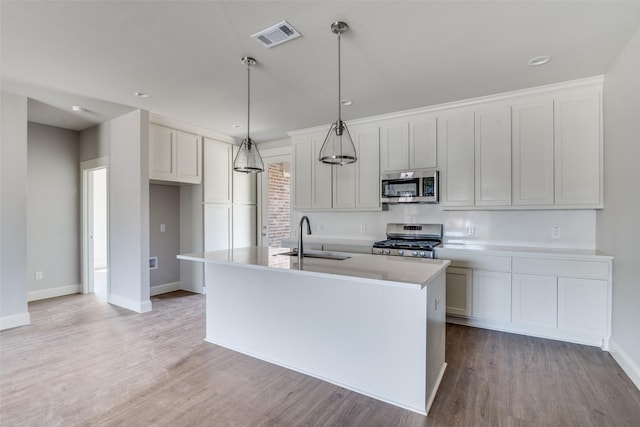 kitchen with a center island with sink, visible vents, appliances with stainless steel finishes, light countertops, and a sink