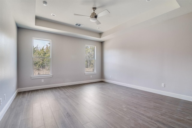 empty room featuring baseboards, visible vents, a ceiling fan, wood finished floors, and a tray ceiling