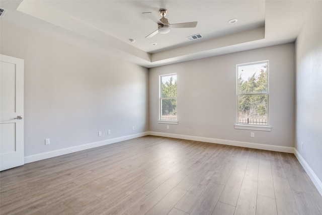 empty room featuring ceiling fan, light wood finished floors, visible vents, and baseboards