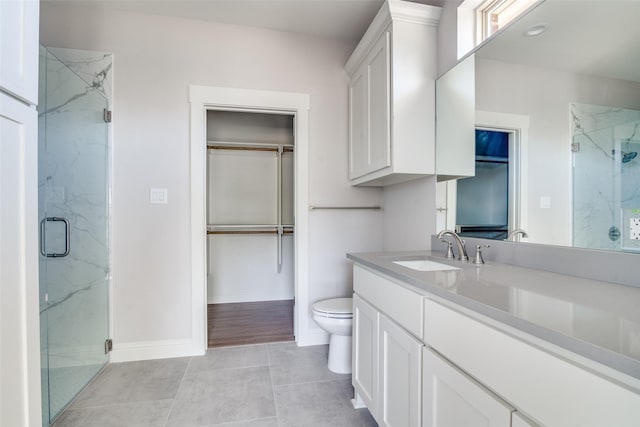 full bathroom featuring a marble finish shower, a spacious closet, toilet, vanity, and baseboards