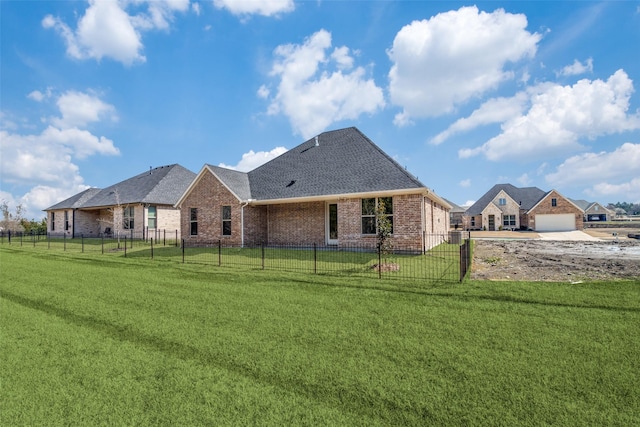 rear view of house featuring a fenced front yard, brick siding, a yard, and a shingled roof