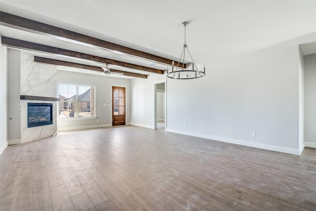 unfurnished living room with beam ceiling, a fireplace, wood finished floors, baseboards, and ceiling fan with notable chandelier