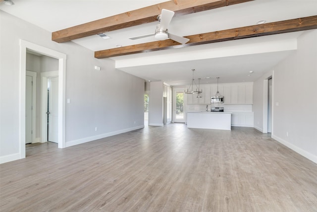 unfurnished living room with beam ceiling, ceiling fan, light wood-style flooring, and baseboards