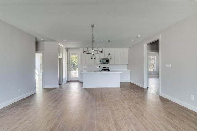 kitchen with white cabinets, hanging light fixtures, appliances with stainless steel finishes, light countertops, and a center island with sink