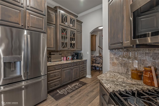 kitchen featuring arched walkways, appliances with stainless steel finishes, glass insert cabinets, and light stone countertops