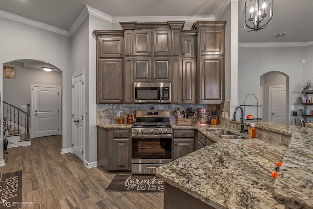 kitchen with arched walkways, dark wood finished floors, stainless steel appliances, a sink, and dark brown cabinets