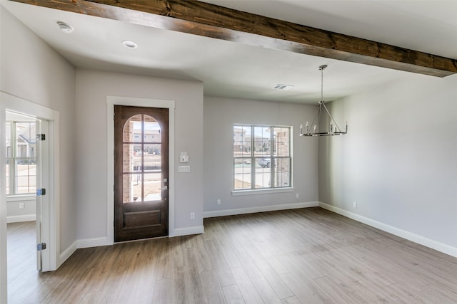 foyer with a healthy amount of sunlight, beam ceiling, light wood-style flooring, and a notable chandelier