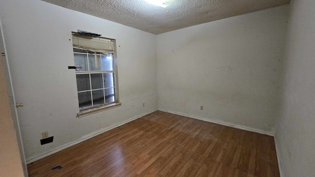 spare room featuring a textured ceiling, wood finished floors, and baseboards