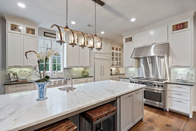 kitchen with pendant lighting, high end appliances, glass insert cabinets, dark stone counters, and under cabinet range hood