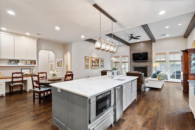 kitchen featuring white cabinets, a kitchen island with sink, open floor plan, and light stone countertops