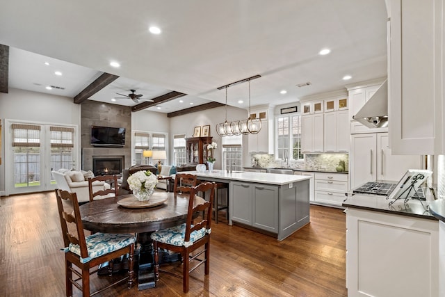 dining area featuring dark wood finished floors, a ceiling fan, a fireplace, beam ceiling, and recessed lighting