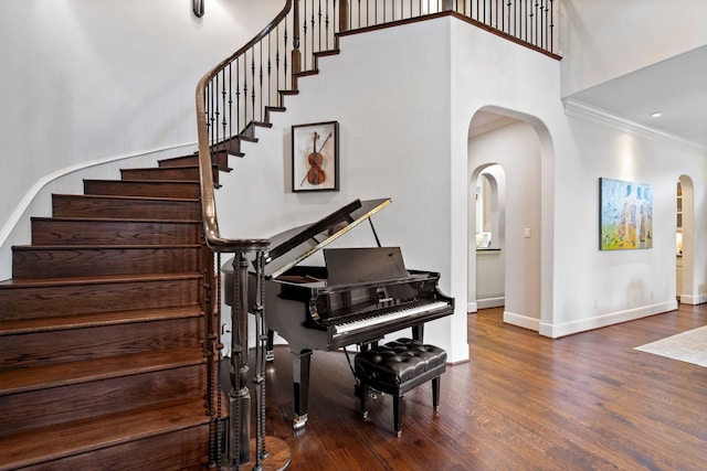 stairway featuring arched walkways, a towering ceiling, ornamental molding, wood finished floors, and baseboards