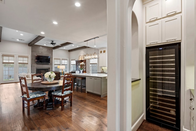 dining room featuring dark wood-type flooring, beverage cooler, a large fireplace, and beam ceiling