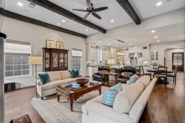 living area with a wealth of natural light, arched walkways, visible vents, and beamed ceiling