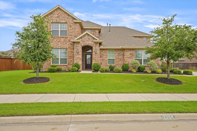 traditional-style home featuring brick siding, a front lawn, a shingled roof, and fence