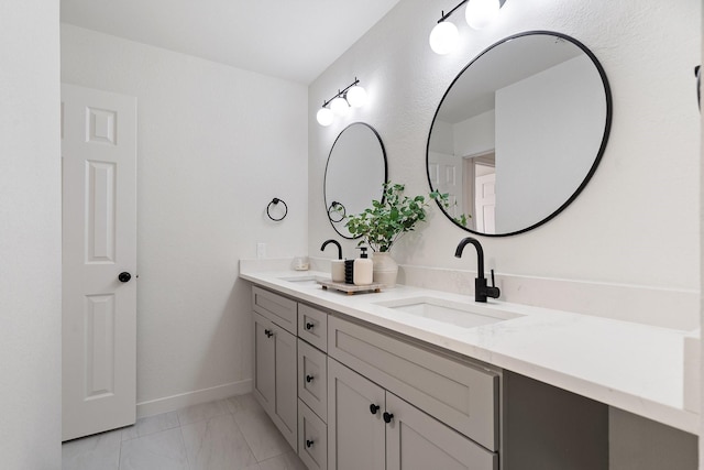 bathroom featuring marble finish floor, double vanity, a sink, and baseboards