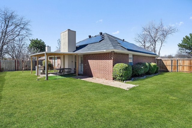 rear view of house featuring brick siding, a chimney, roof mounted solar panels, a patio area, and a fenced backyard