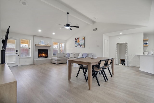 dining space featuring vaulted ceiling with beams, light wood finished floors, visible vents, and a large fireplace