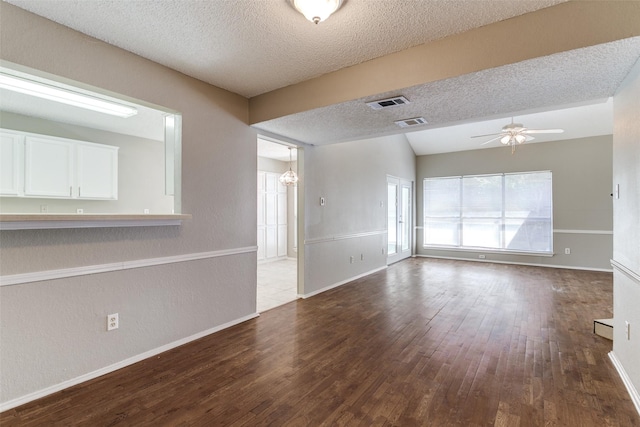 unfurnished room with a textured ceiling, visible vents, dark wood-type flooring, and ceiling fan with notable chandelier