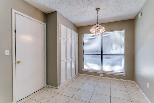 unfurnished dining area with light tile patterned flooring, a notable chandelier, a textured ceiling, and baseboards