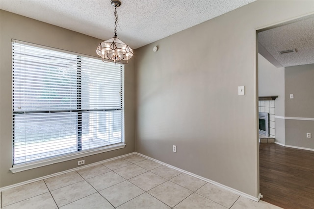 unfurnished room with visible vents, a tiled fireplace, a textured ceiling, light tile patterned floors, and a chandelier