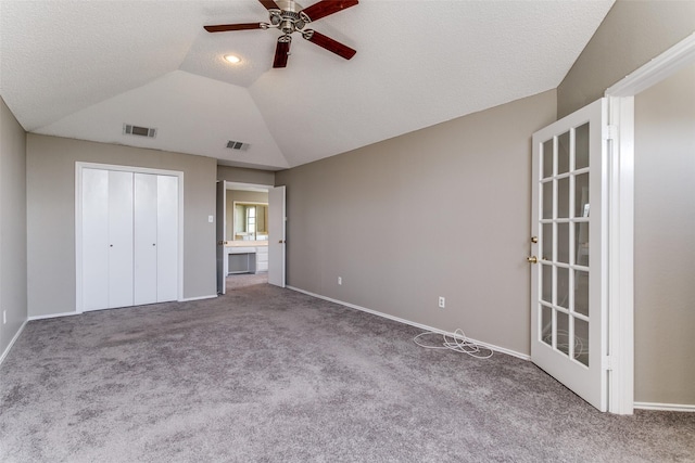 unfurnished bedroom featuring visible vents, carpet floors, lofted ceiling, ceiling fan, and a textured ceiling