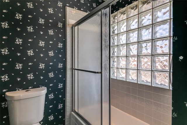 bathroom featuring wallpapered walls, toilet, and a shower with shower door