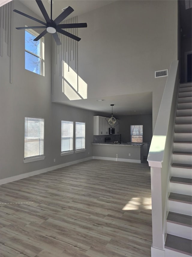 unfurnished living room featuring light wood finished floors, visible vents, baseboards, stairway, and a high ceiling