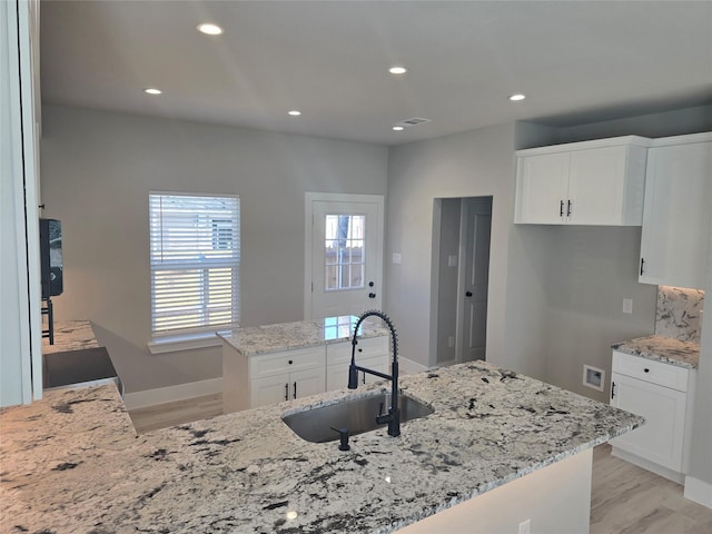 kitchen with white cabinets, a sink, and light stone countertops