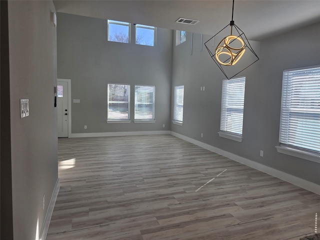 unfurnished room with light wood-type flooring, a towering ceiling, visible vents, and baseboards