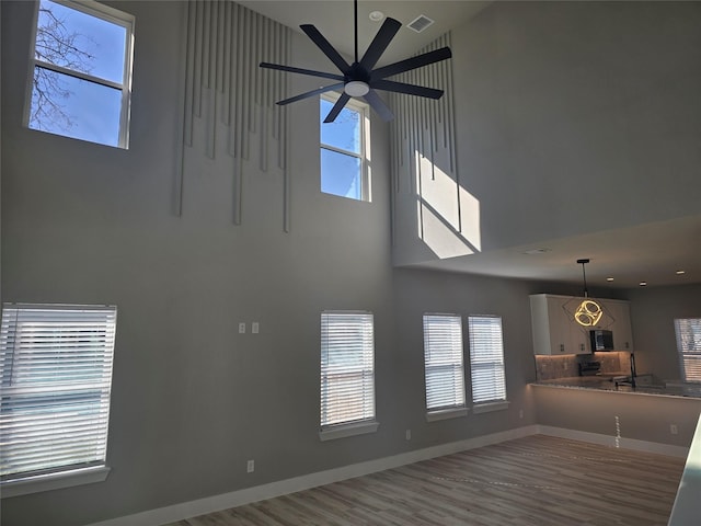 unfurnished living room featuring a high ceiling, wood finished floors, a ceiling fan, visible vents, and baseboards