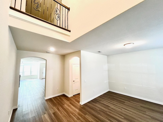 empty room featuring baseboards, visible vents, arched walkways, dark wood finished floors, and a textured ceiling