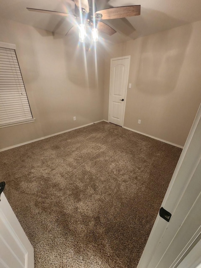 carpeted spare room featuring ceiling fan and baseboards