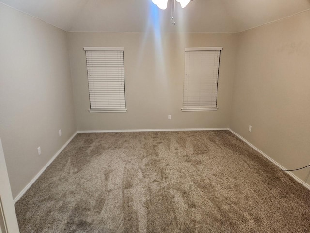 carpeted empty room featuring lofted ceiling and baseboards