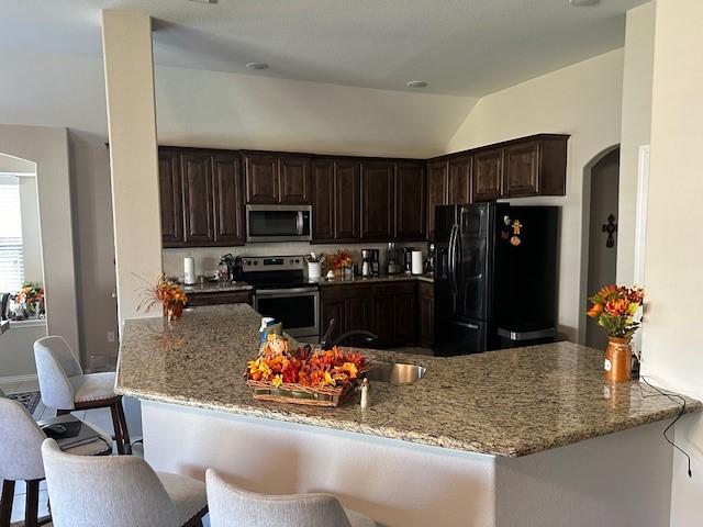 kitchen featuring stainless steel appliances, a peninsula, light stone countertops, and a kitchen breakfast bar