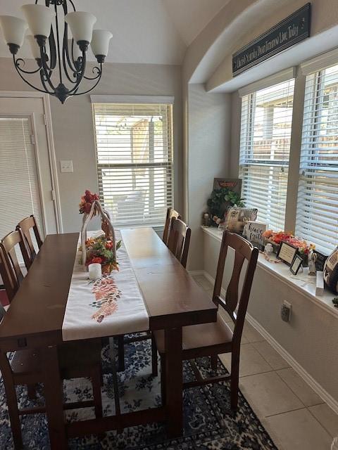 tiled dining area with a chandelier, vaulted ceiling, and baseboards