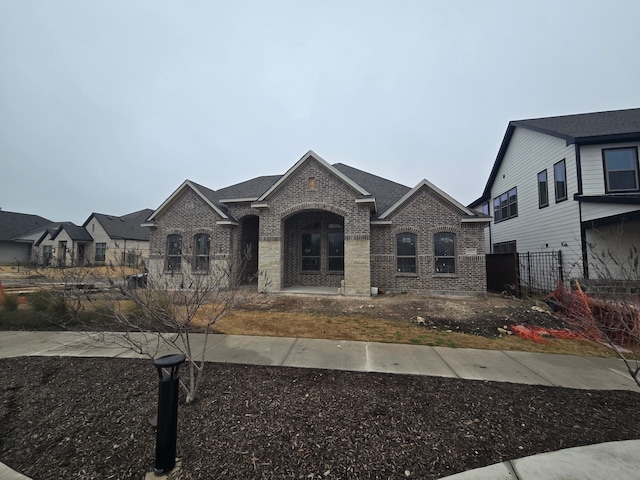 view of front of property with brick siding, roof with shingles, fence, and a residential view