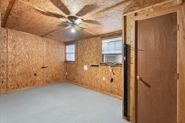 unfurnished room featuring wood walls, finished concrete floors, cooling unit, a ceiling fan, and baseboards