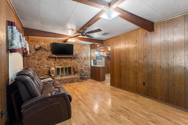 living room with light wood-style flooring, wooden walls, a fireplace, visible vents, and beam ceiling