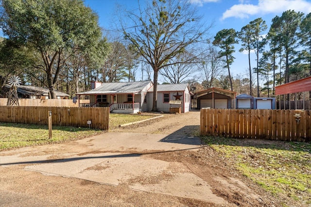 bungalow-style home with covered porch, a detached garage, an outbuilding, metal roof, and a fenced front yard