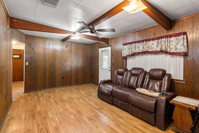 living area featuring wooden walls, wood finished floors, visible vents, and beam ceiling