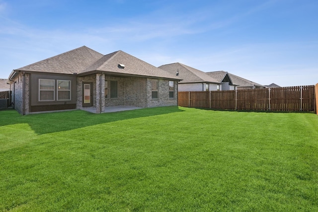 rear view of house with brick siding, a fenced backyard, and a yard