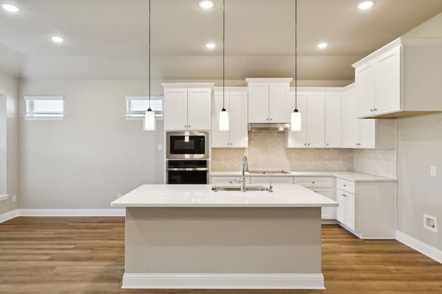 kitchen featuring decorative light fixtures, stainless steel oven, light countertops, white cabinetry, and a sink