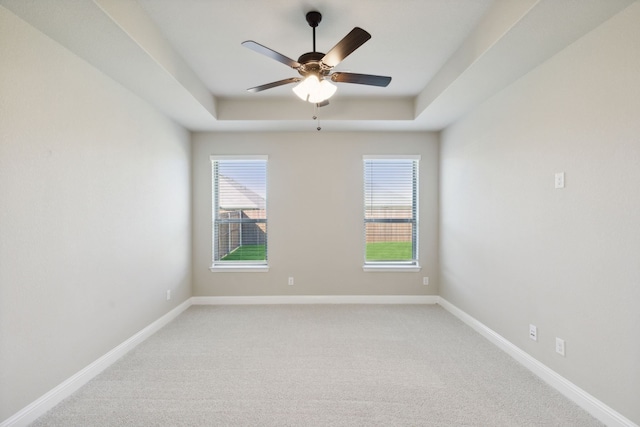 unfurnished room featuring ceiling fan, a tray ceiling, light colored carpet, and baseboards