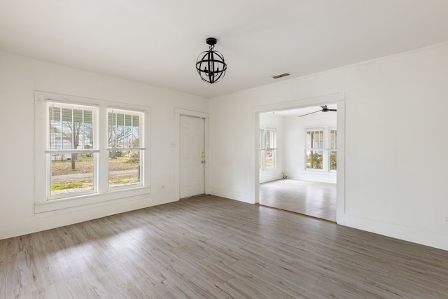 empty room featuring visible vents, a notable chandelier, baseboards, and wood finished floors